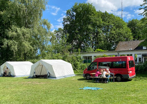zwei zelte und ein kleinbus vor einem freizeitheim auf einer wiese