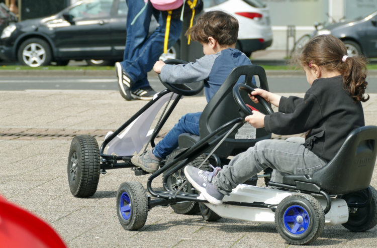 zwei-kinder-fahren-draussen-mit-kettcars