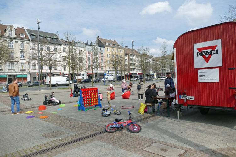 kinder-und-erwachsene-mit-spielsachen-neben-einem-roten-bauwagen