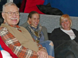 Ein älterer Mann sitzt neben zwei jungen Frauen