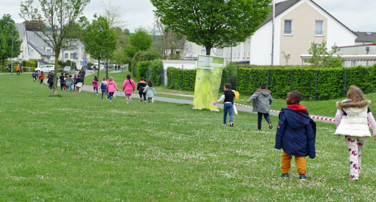 Kinder laufen über eine Wiese neben einem Radweg