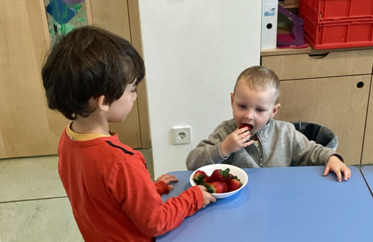 Kinder sitzen am Tisch in der Kita und essen Erdbeeren