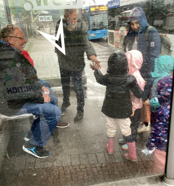 Kinder ueberreichen Passanten an einer Bushaltestelle kleine Beutel
