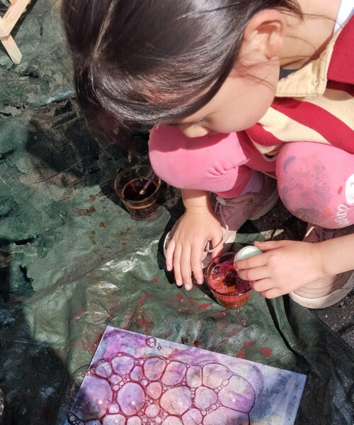 Ein Kinder hockt auf einer Plane und kreiert aus Wasser und Farbe ein Bubble-Bild